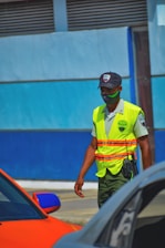 man in yellow and green safety vest and helmet standing beside blue car during daytime