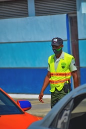 man in yellow and green safety vest and helmet standing beside blue car during daytime
