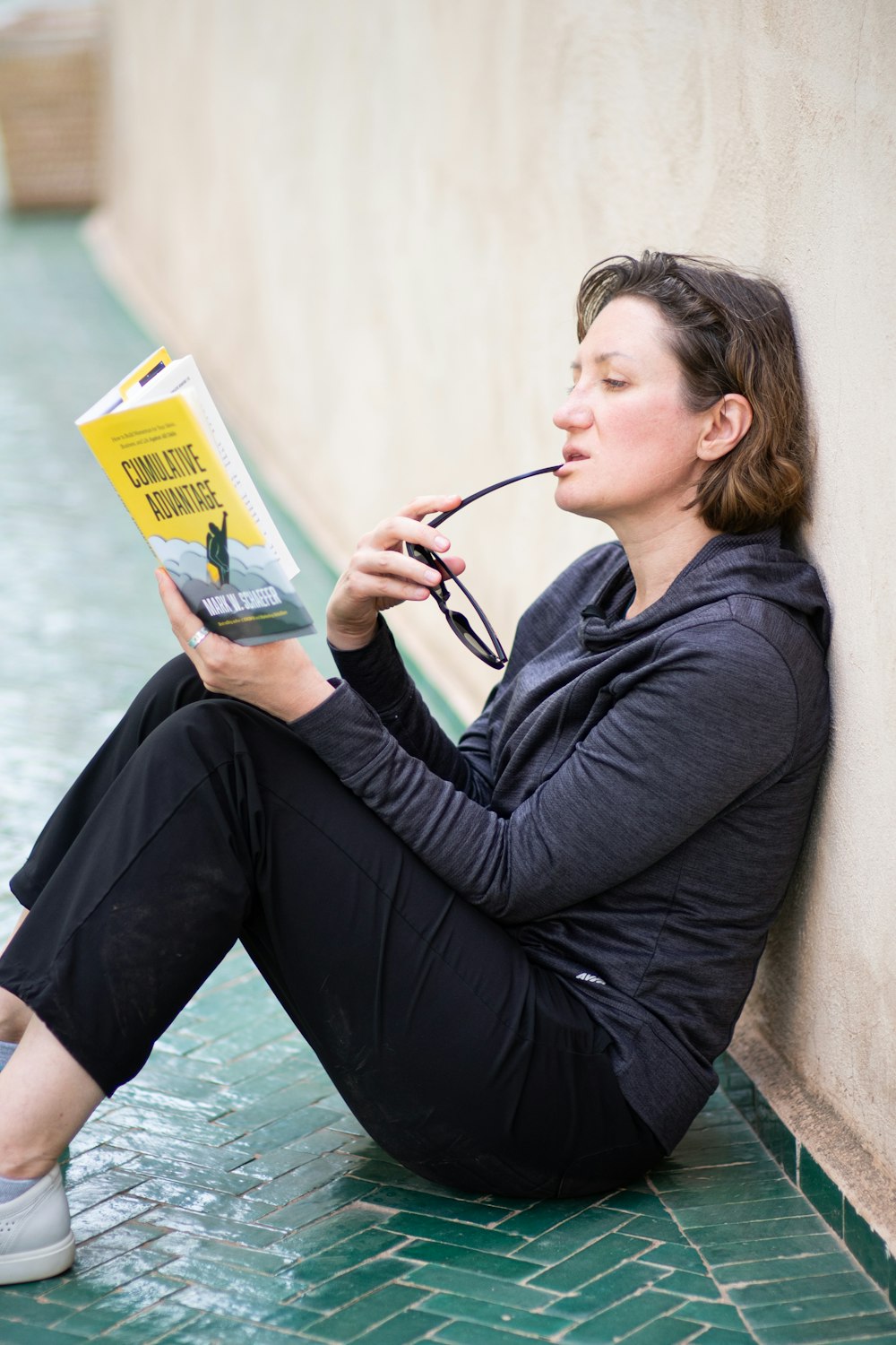 woman in black long sleeve shirt sitting on concrete bench while reading book