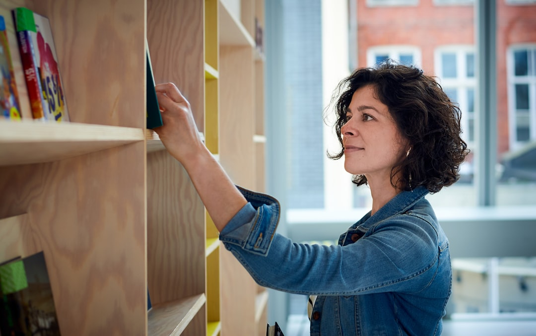 Young woman in blue jacket choosing a book from a bookshelves