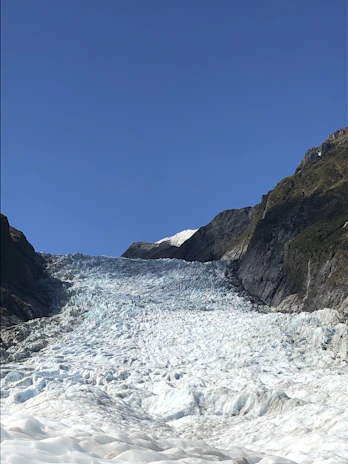 Stunning scenic shot of a glacier flowing into a crystal-clear river under a bright sky.