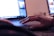 A person's hand is resting on the touchpad of a laptop, suggesting interaction with the device. The screen displays a bright interface, likely a graphic design or editing program. In the background, there is another computer screen visible, partially blurred.