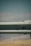 A metal guardrail is positioned horizontally across the image, with visible bolts and a slightly rustic texture. The background features a blurred landscape of hills and a blue sky, creating a muted, serene backdrop.
