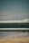 A metal guardrail is positioned horizontally across the image, with visible bolts and a slightly rustic texture. The background features a blurred landscape of hills and a blue sky, creating a muted, serene backdrop.