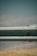 A metal guardrail is positioned horizontally across the image, with visible bolts and a slightly rustic texture. The background features a blurred landscape of hills and a blue sky, creating a muted, serene backdrop.