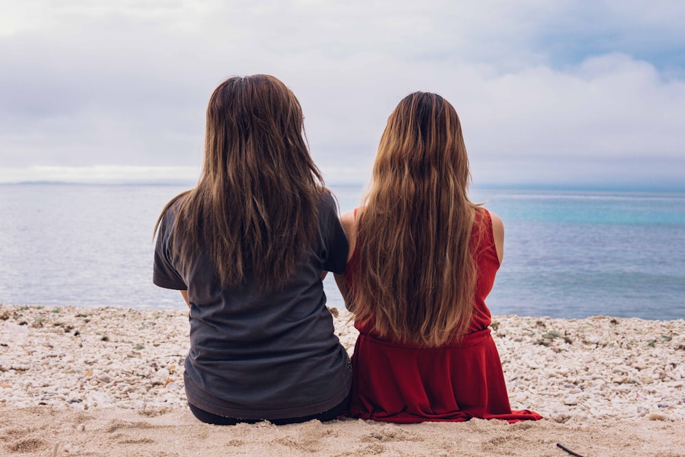 2 women sitting on beach during daytime