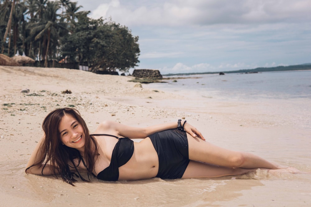 woman in black bikini lying on beach sand during daytime