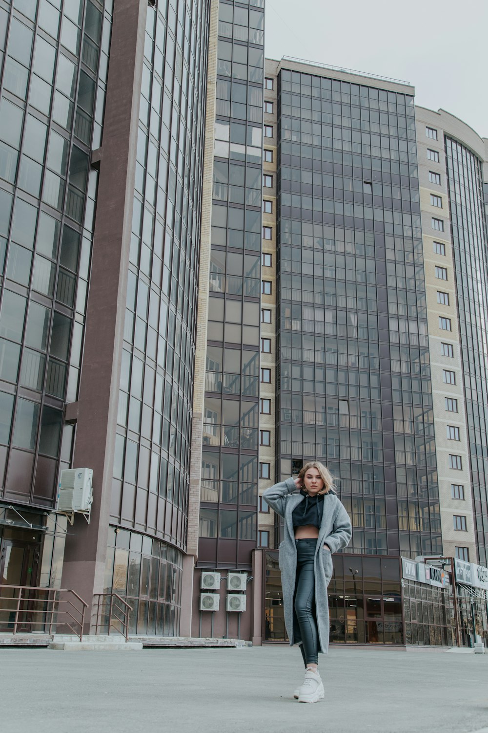 woman in gray jacket standing near high rise building during daytime