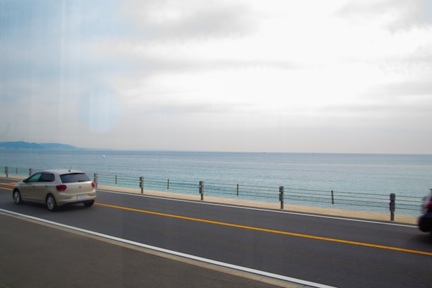 A sunny coastal road in Mayotte with a rental car driving along the lagoon.