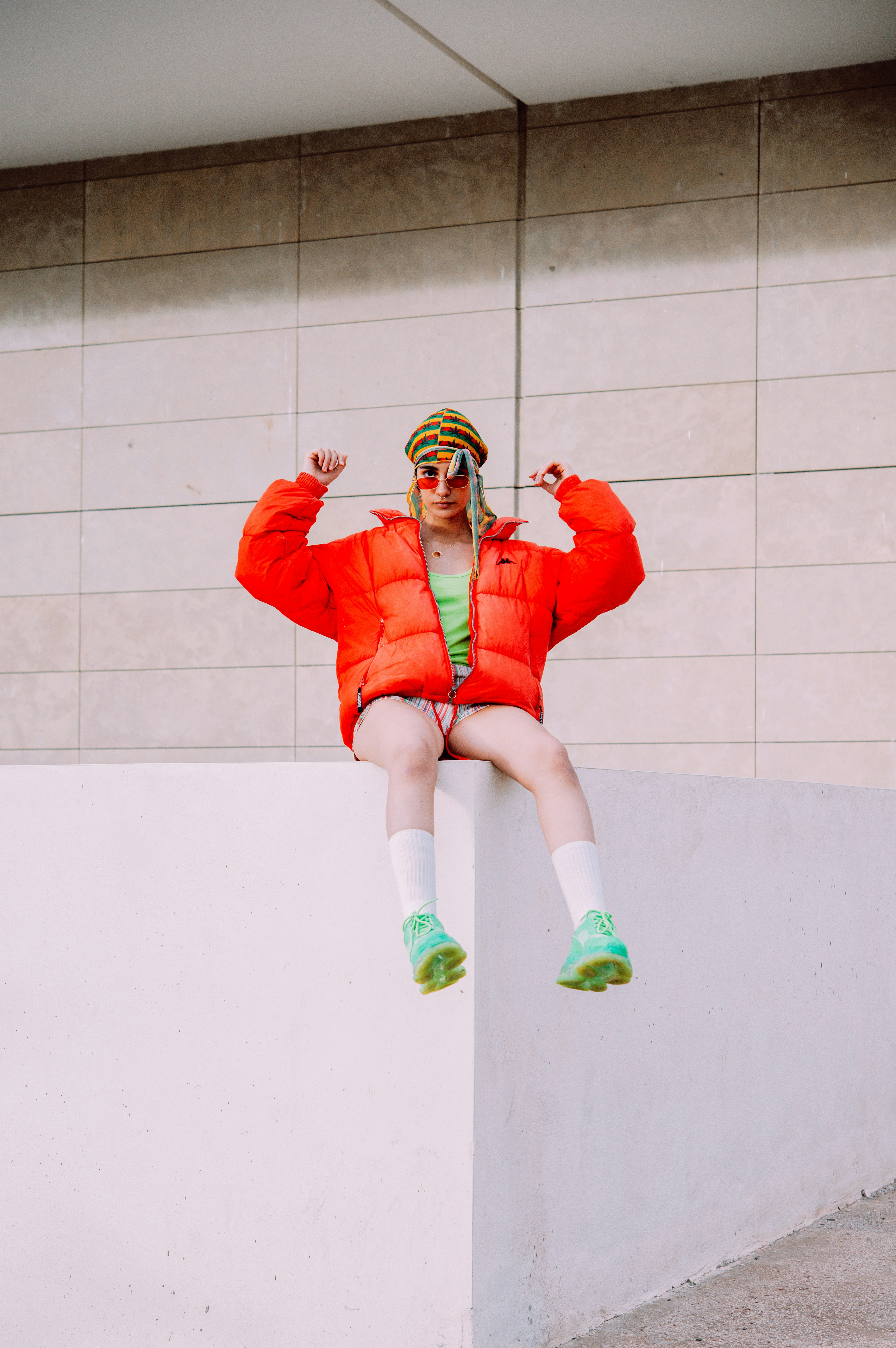 a woman in a red jacket and green shoes sitting on a wall