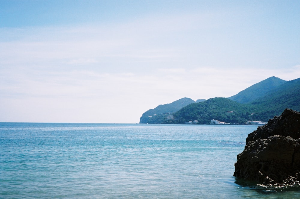 昼間の白い空の下の海に黒い岩層