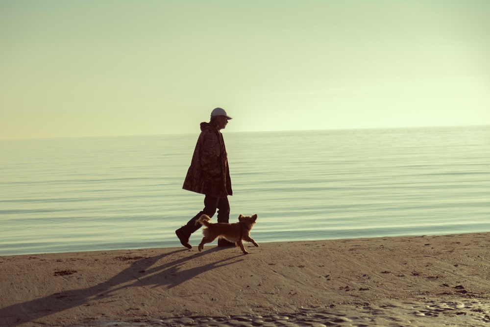 Frau im schwarzen Mantel steht tagsüber neben braunem Kurzmantelhund am Strand