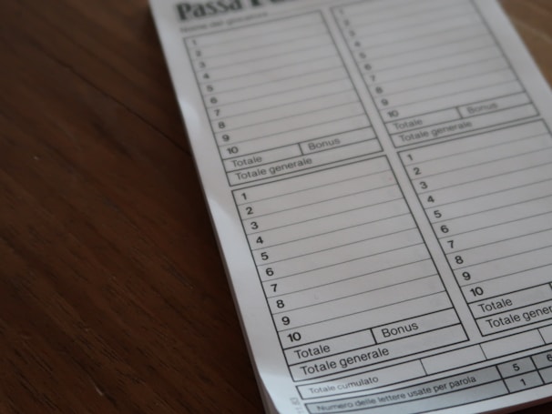 A close-up view of a game score sheet labeled 'Passa Parola'. The sheet is divided into columns with numbered rows for recording scores, marked with 'Totale' and 'Bonus'. It is placed on a wooden surface.