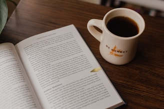 white book beside white ceramic mug on brown wooden table