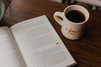 white book beside white ceramic mug on brown wooden table