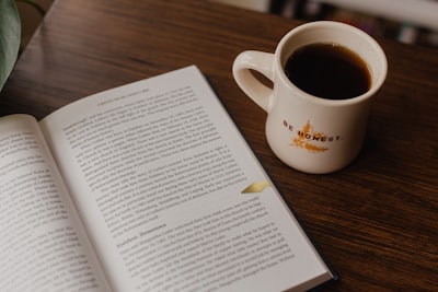 white book beside white ceramic mug on brown wooden table honest zoom background