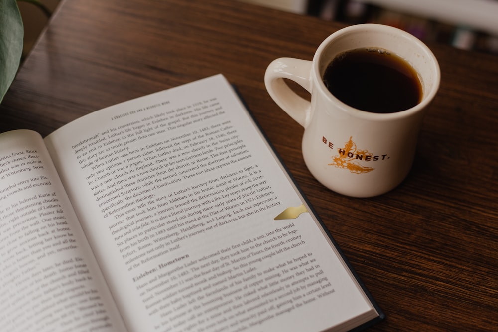 white book beside white ceramic mug on brown wooden table