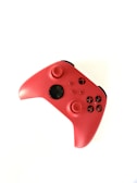 A vibrant red gaming controller featuring black buttons and directional sticks. The controller has an ergonomic design and appears to be for a modern gaming console, possibly an Xbox.