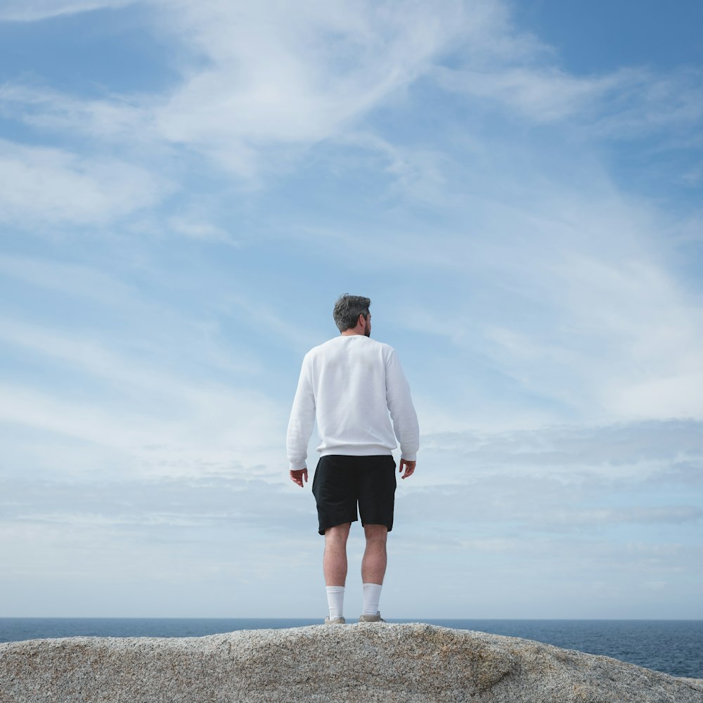 man in white long sleeve shirt and black shorts standing on gray rock formation during daytime