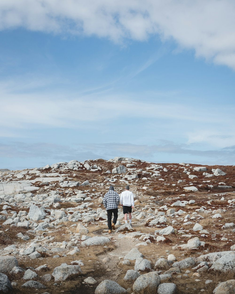 man and woman walking on rocky hill under blue sky during daytime
