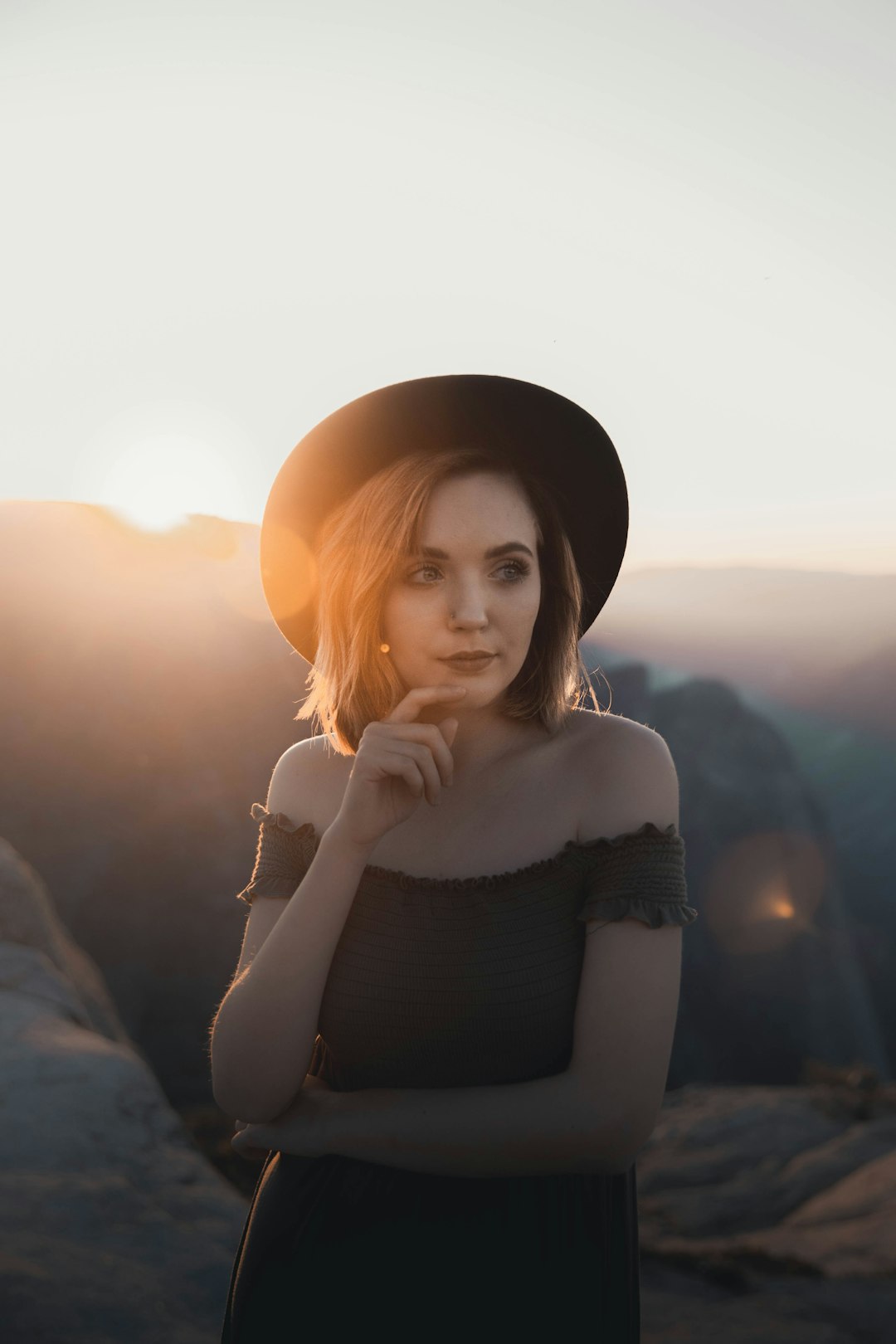 woman in black tank top and black hat sitting on rock during sunset