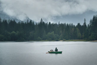 A serene Finnish lake at dawn with a person fishing from a small boat surrounded by misty forest.
