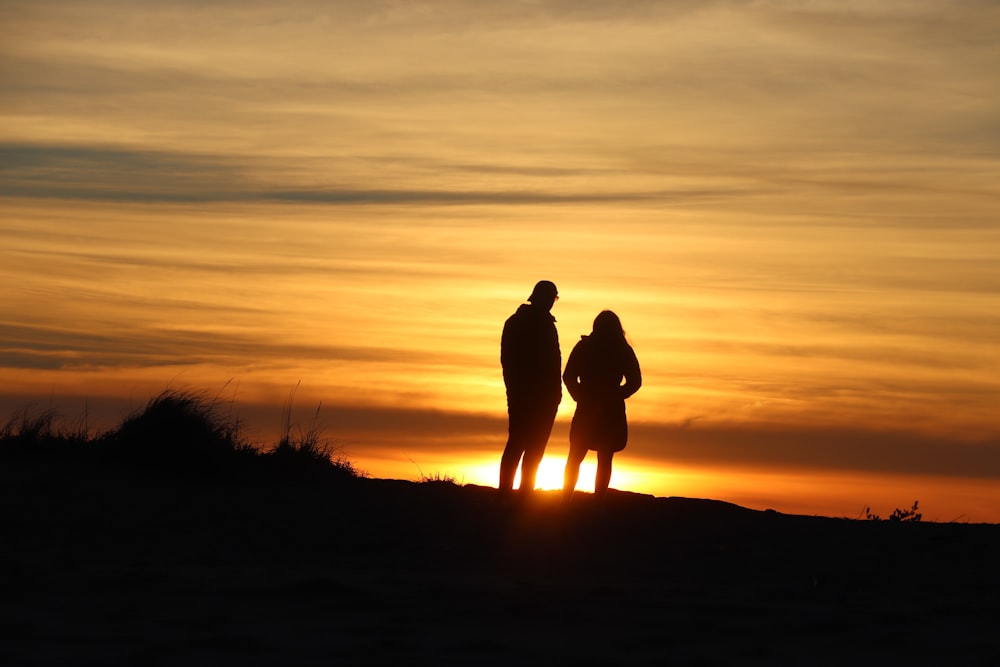 silhouette of man and woman standing on grass field during sunset