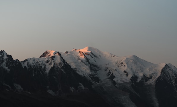 Golden sunrise casting warm light on snow-capped Alpine peaks with a clear blue sky.