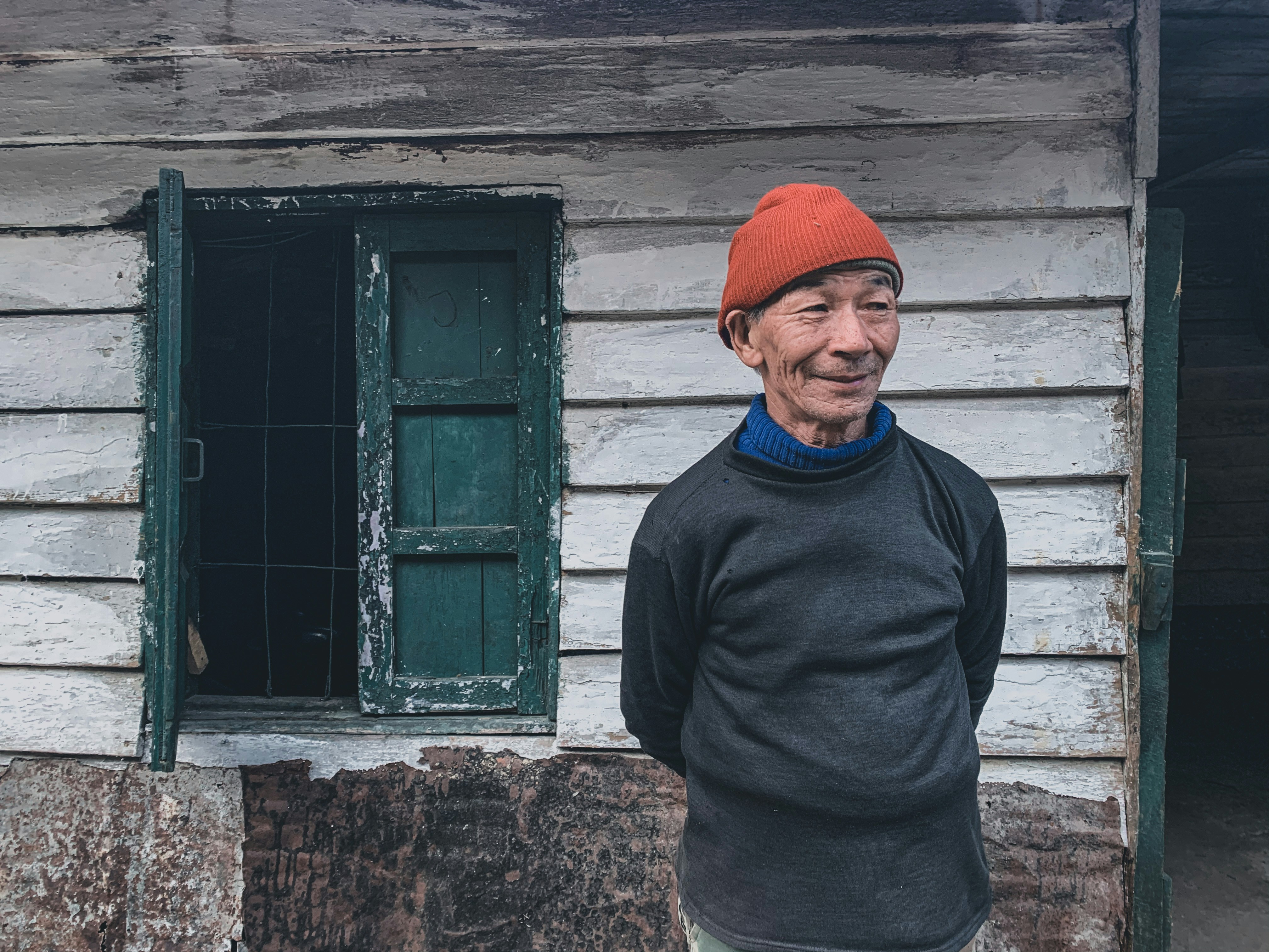 man in black sweater standing beside green wooden window