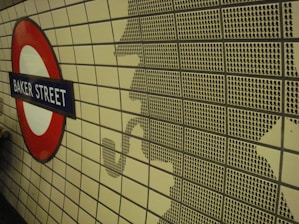 A tiled wall features a silhouette made up of smaller black tile patterns, resembling a detective smoking a pipe. To the left, a circular London Underground sign with 'Baker Street' written on a blue background stands out.