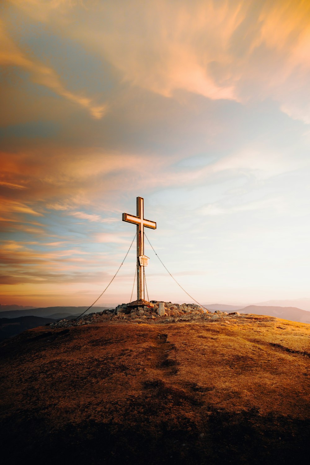 white cross on brown hill under white clouds and blue sky during daytime