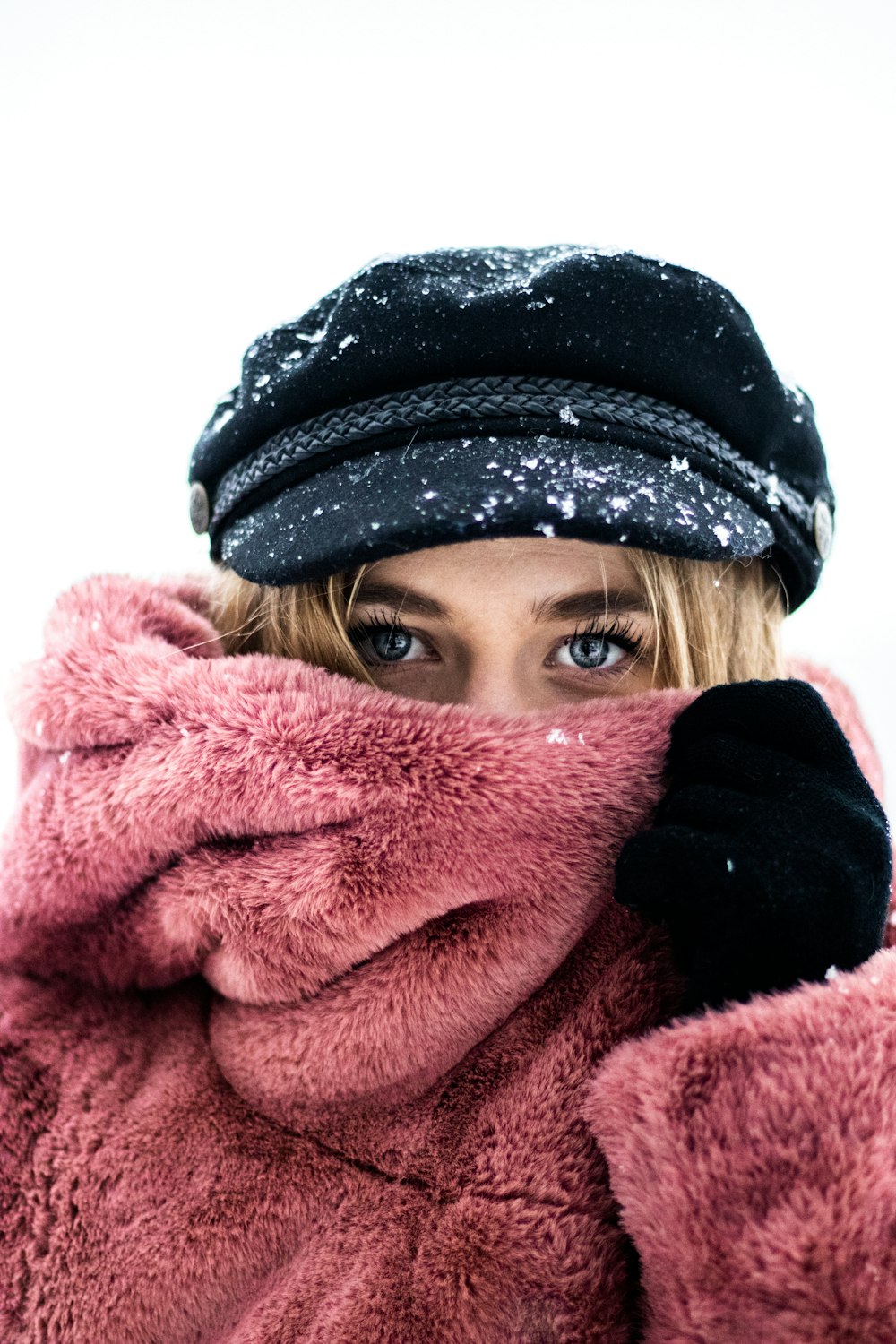 woman in black knit cap covering her face with pink blanket