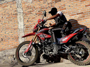 A biker wearing rugged, edgy vėjasriba apparel leaning against a classic motorcycle at sunset.