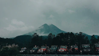 A convoy of motorcycles and 4x4s winding through a misty mountain pass at dawn.