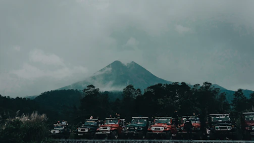A convoy of motorcycles and 4x4s winding through a misty mountain pass at dawn.