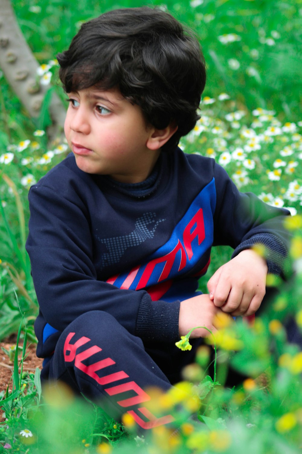 boy in black and red adidas sweater sitting on green grass during daytime