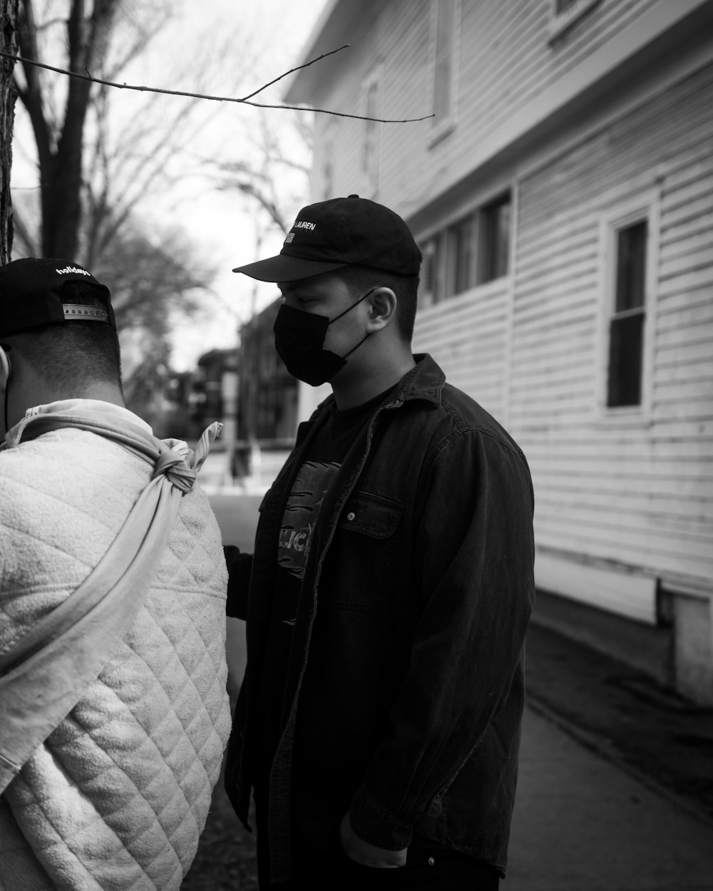 man in black jacket and black cap standing near white wooden house during daytime