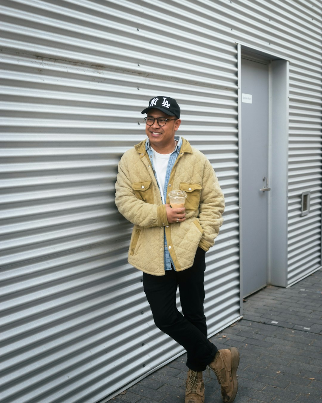 man in yellow button up jacket and black pants standing beside white wall