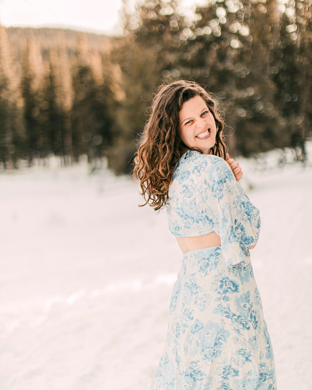 Mujer en vestido floral blanco y rojo de pie en el suelo cubierto de nieve durante el día