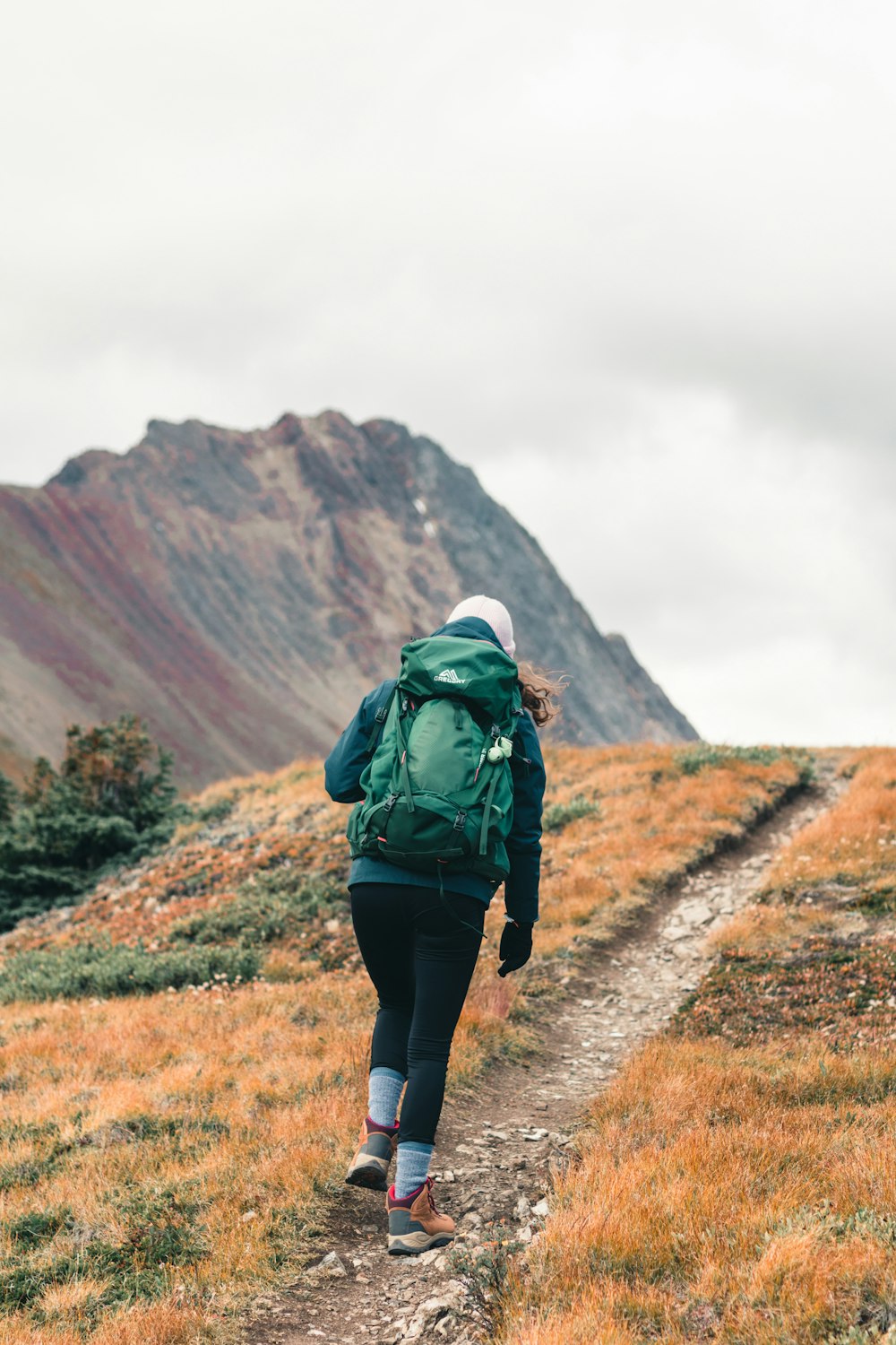 personne en veste verte et pantalon noir marchant sur un champ d’herbe brune pendant la journée