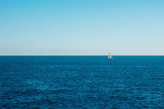 A lone sailboat cutting through deep blue waters under a clear sky.