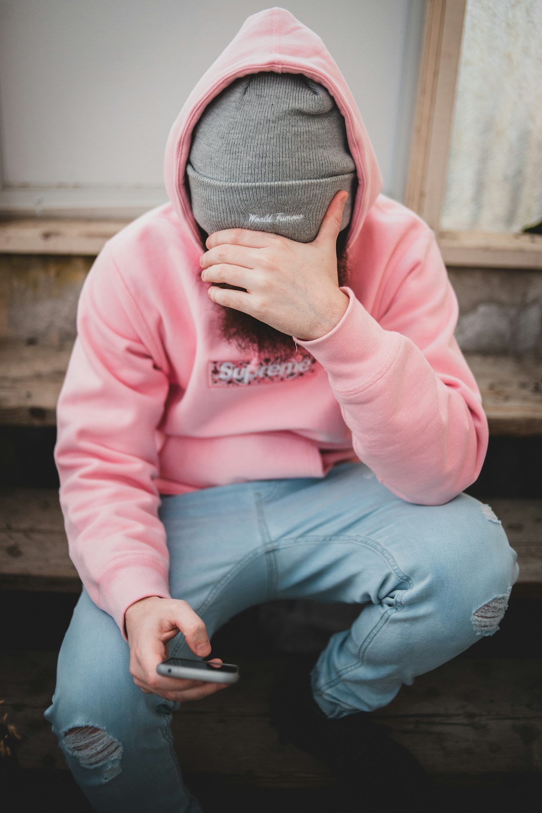 person in pink jacket and gray knit cap sitting on brown wooden bench