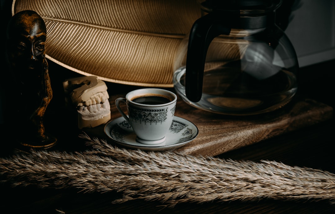 white ceramic mug on white ceramic saucer beside black coffee maker