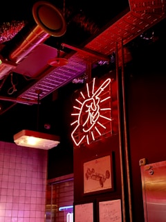 A bold orange neon sign glowing 'stefange: asfalto y grasa' inside a dark, steel-themed workshop