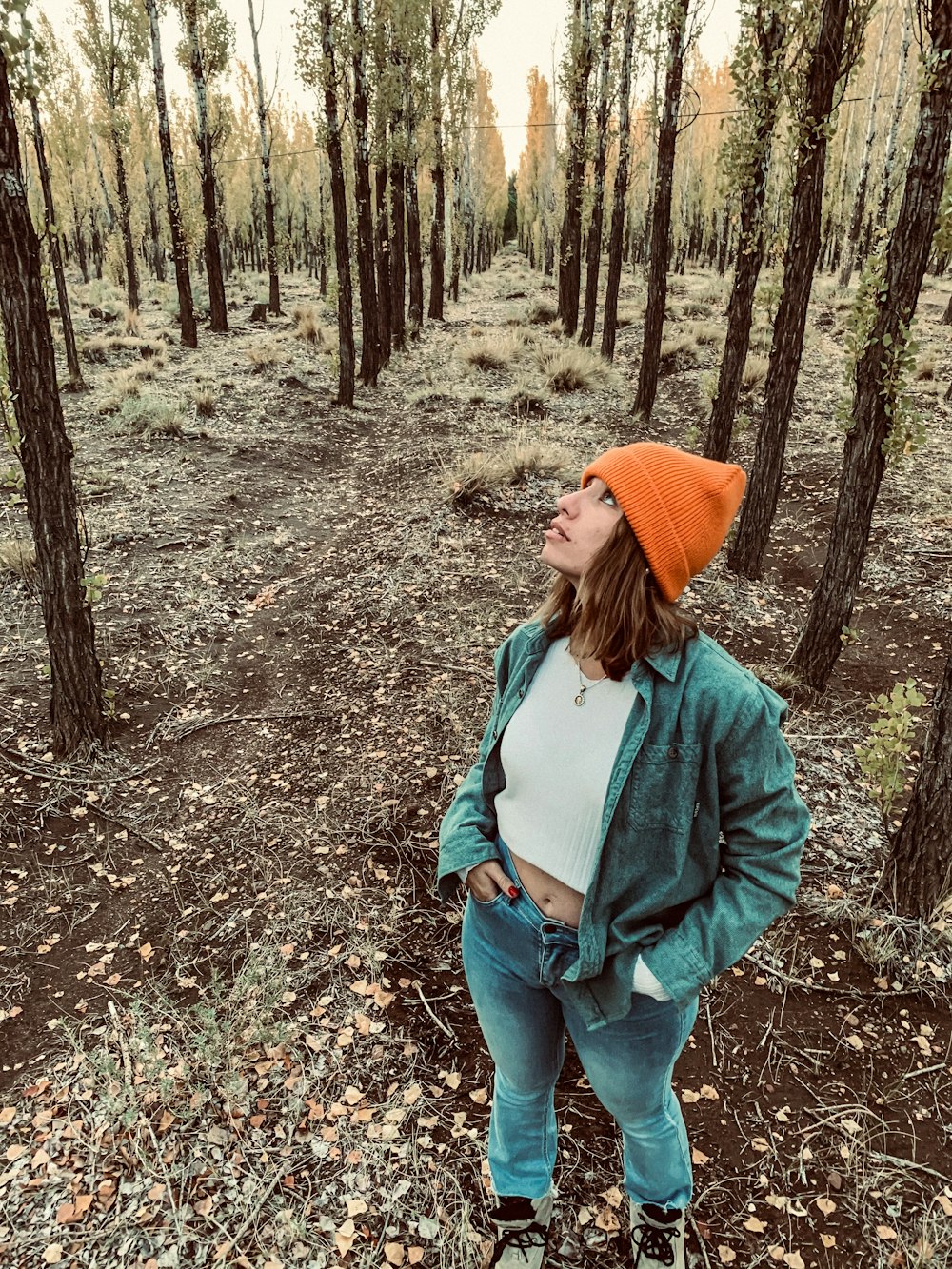 woman in green jacket and orange knit cap standing in the woods
