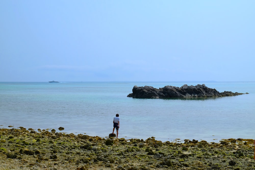 2 person standing on brown rock near body of water during daytime