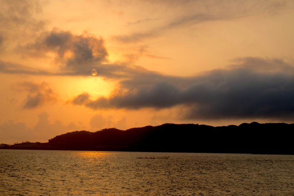 silhouette of mountain near body of water during sunset