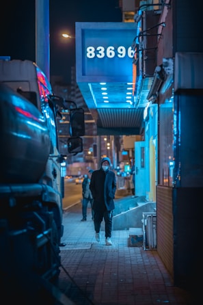 Urban night scene with a person wearing a charcoal hoodie illuminated by neon city lights.