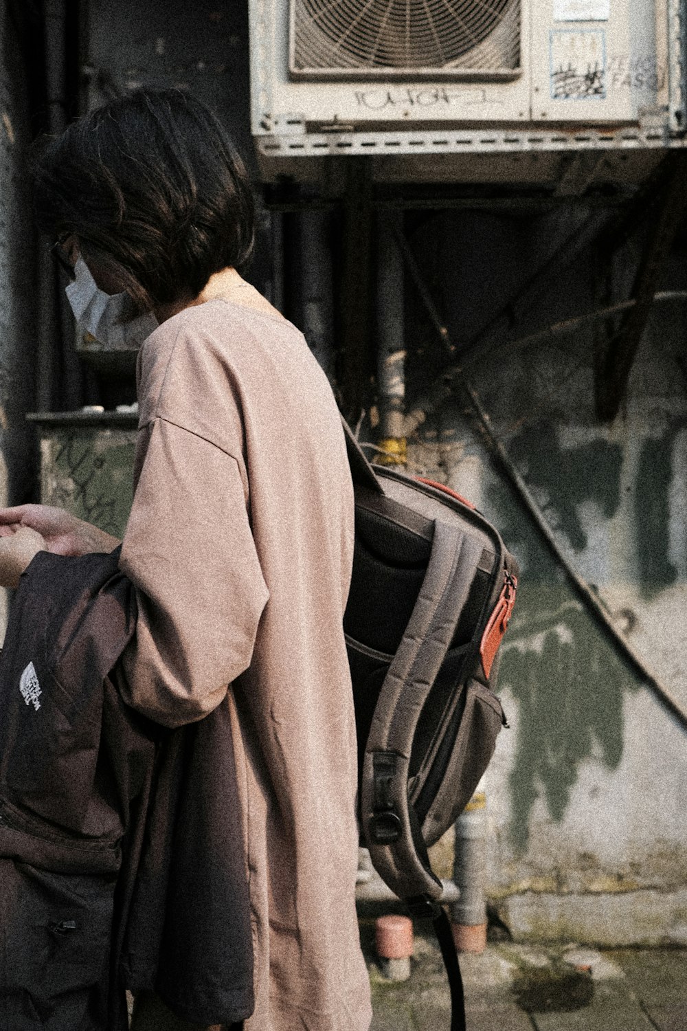 woman in beige coat standing beside black and red backpack