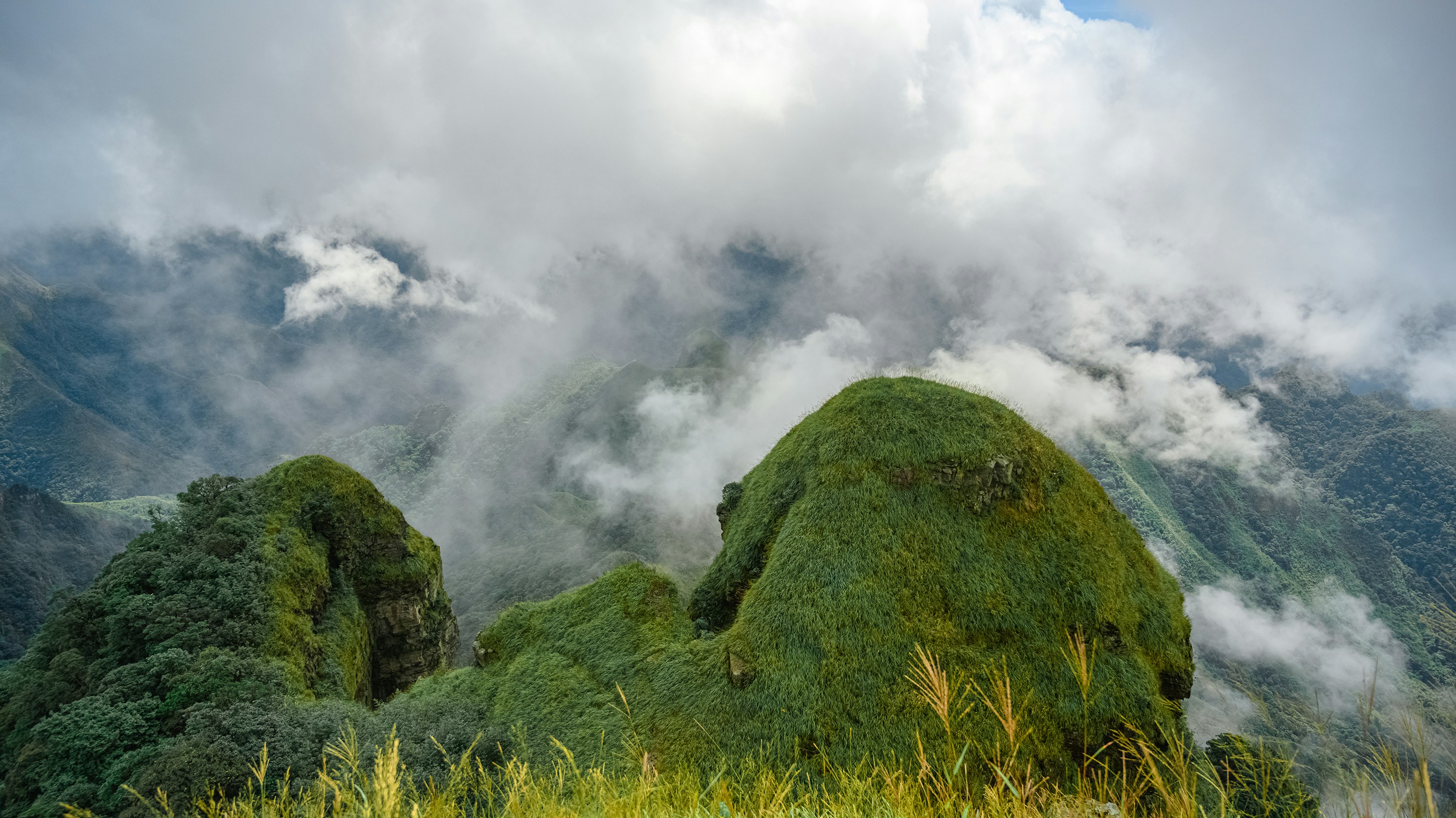 green grass covered mountain under white clouds during daytime
